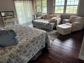 Een slaapkamer met een groot bed, een bank, een voetenbankje en een raam met uitzicht op het omliggende landschap.