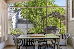 A covered patio with a table and chairs, large windows, and a view of trees and a building. - Spacious 4-bedroom modern cottage in beautiful Prescott with AC and large yard (Prescott)