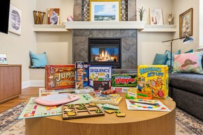 A living room with a fireplace, a coffee table with board games, and a sofa. - Spacious 4-bedroom modern cottage in beautiful Prescott with AC and large yard (Prescott)
