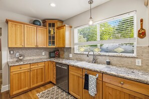 A kitchen with wooden cabinets, a dishwasher, a granite countertop, a window with blinds, and a hanging light fixture. - Spacious 4-bedroom modern cottage in beautiful Prescott with AC and large yard (Prescott)