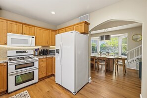 A kitchen with wooden cabinets, a white refrigerator, a microwave, and a stove. - Spacious 4-bedroom modern cottage in beautiful Prescott with AC and large yard (Prescott)
