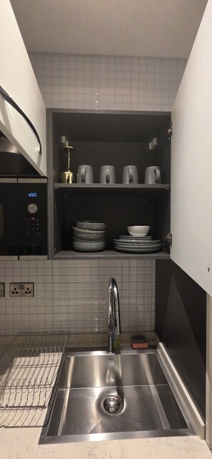 A modern kitchen with a built-in microwave, a stainless steel sink, and a shelf with dishes and cups. - signature Apartments Exquisite (Accra)