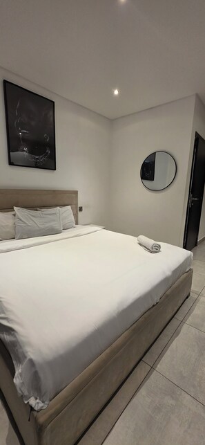 Ein modernes Hotelzimmer mit einem großen Bett, einem Kopfteil, einem wandmontierten Spiegel und einem Gemälde.