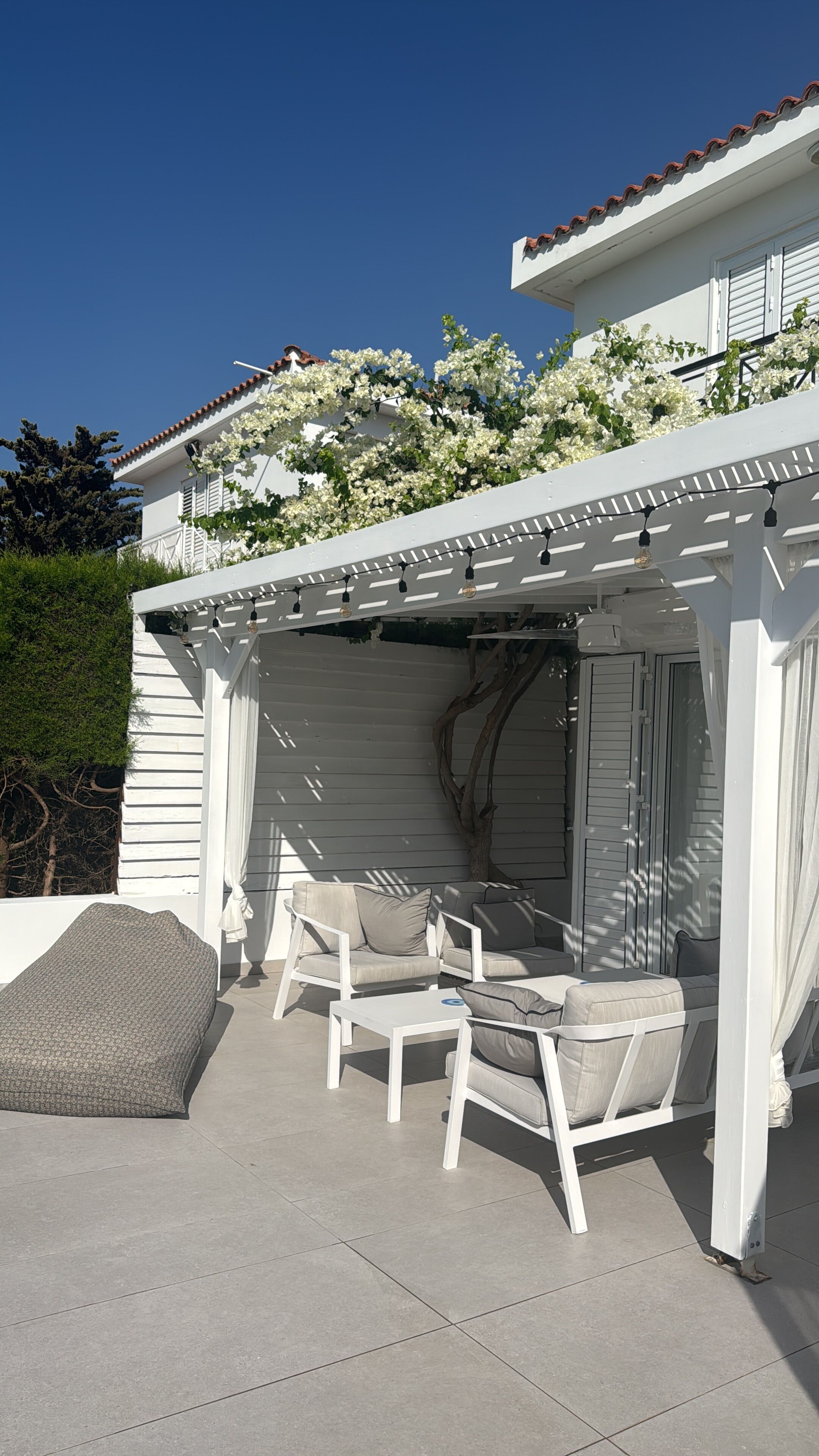 Een overdekt terras met witte meubels en een pergola.