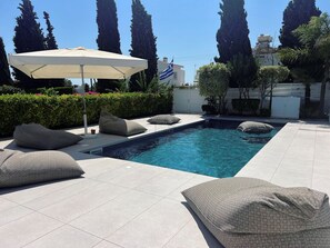 A swimming pool with a tiled deck, a lounge chair, and an umbrella. - Protaras Cyprus Beach House (Paralimni)