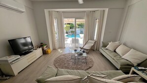 Een moderne woonkamer met een bank, televisie en uitzicht op een zwembad.