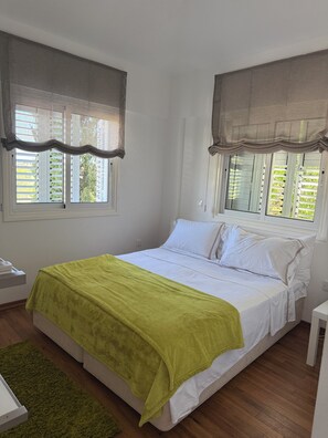 Une chambre à coucher avec un lit, deux fenêtres avec des rideaux, une table de chevet et un tapis vert.