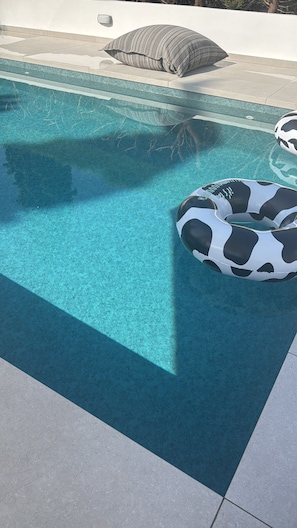 Une piscine avec une eau d’un bleu limpide, un flotteur gonflable noir et blanc, et un coussin gris posé sur le bord.