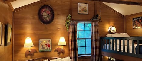 A wooden cabin room with a bunk bed, two wall-mounted lamps, a window with plaid curtains, and a poster of 'Sleeping Beauty'.