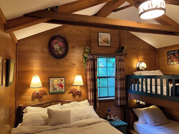 A wooden cabin room with a bunk bed, two wall-mounted lamps, a window with plaid curtains, and a poster of 'Sleeping Beauty'.