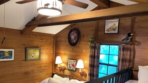 A wooden cabin bedroom with a bed, two wall-mounted lamps, a window with curtains, and a ceiling fan.