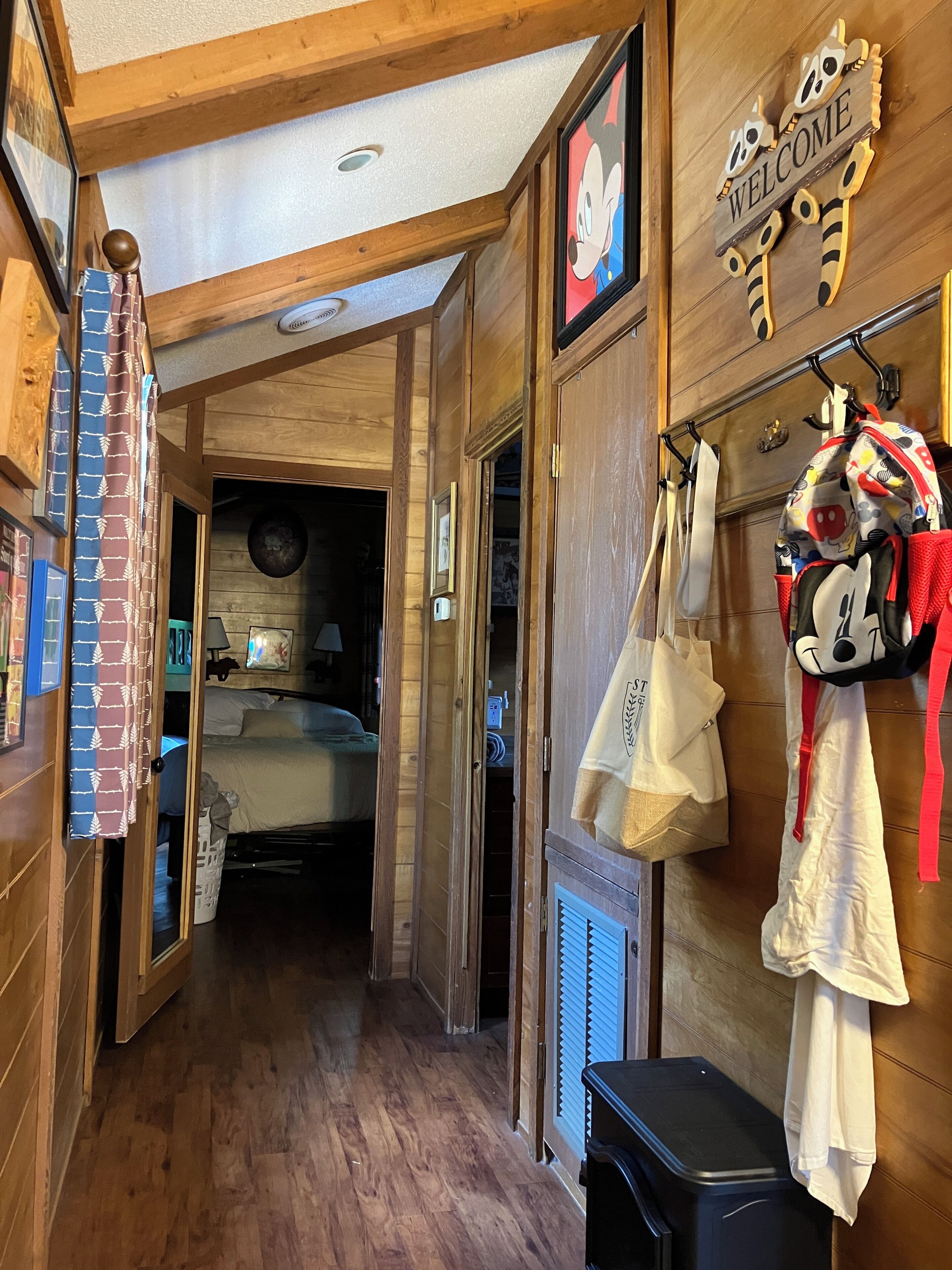 Un couloir intérieur en bois, avec un lit, une pancarte de bienvenue et un porte-manteau avec des sacs.