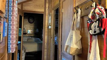 Un couloir intérieur en bois, avec un lit, une pancarte de bienvenue et un porte-manteau avec des sacs.