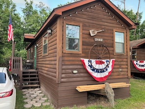 A wooden cabin with a number '2402' on the front, a porch with a bench, and an American flag. - Authentic Fort Wilderness family cabin from Walt Disney World, 1/3 Disney prices (Kissimmee)