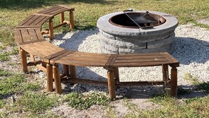A fire pit with a circular stone design and a wooden bench and table set around it.