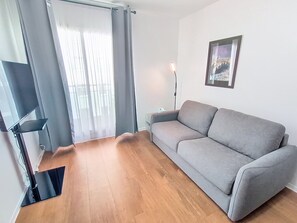 Ein Wohnzimmer mit grauem Sofa, Holzboden, einem TV-Schrank und einem gerahmten Bild an der Wand.