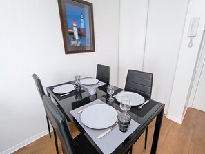 A dining table set for two with chairs, a framed picture of a lighthouse, and a white wall. -  Escapade à Antibes avec Piscine Rooftop (Antibes)