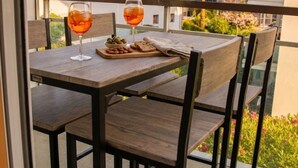 En balkon med et bord dækket til to personer, med et glas rødvin, en tallerken med oliven og en skål med nødder.