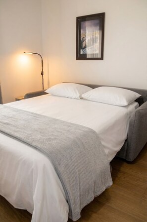 A neatly made bed with white linens, a gray blanket, and a gray pillow. A floor lamp is on the left side of the bed. -  Escapade à Antibes avec Piscine Rooftop (Antibes)
