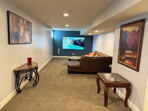 A living room with a flat-screen TV, a brown leather couch, a glass coffee table, and a red vase on a console table. - Modern Luxury Basement Suite-Cozy, Quiet & Stylish (Culpeper)