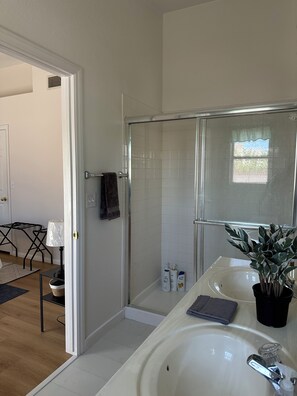 A bathroom with a glass shower enclosure, a sink with a mirror, and a potted plant. - Clean and Cozy 3-bedroom house in peaceful Henderson with AC (henderson)