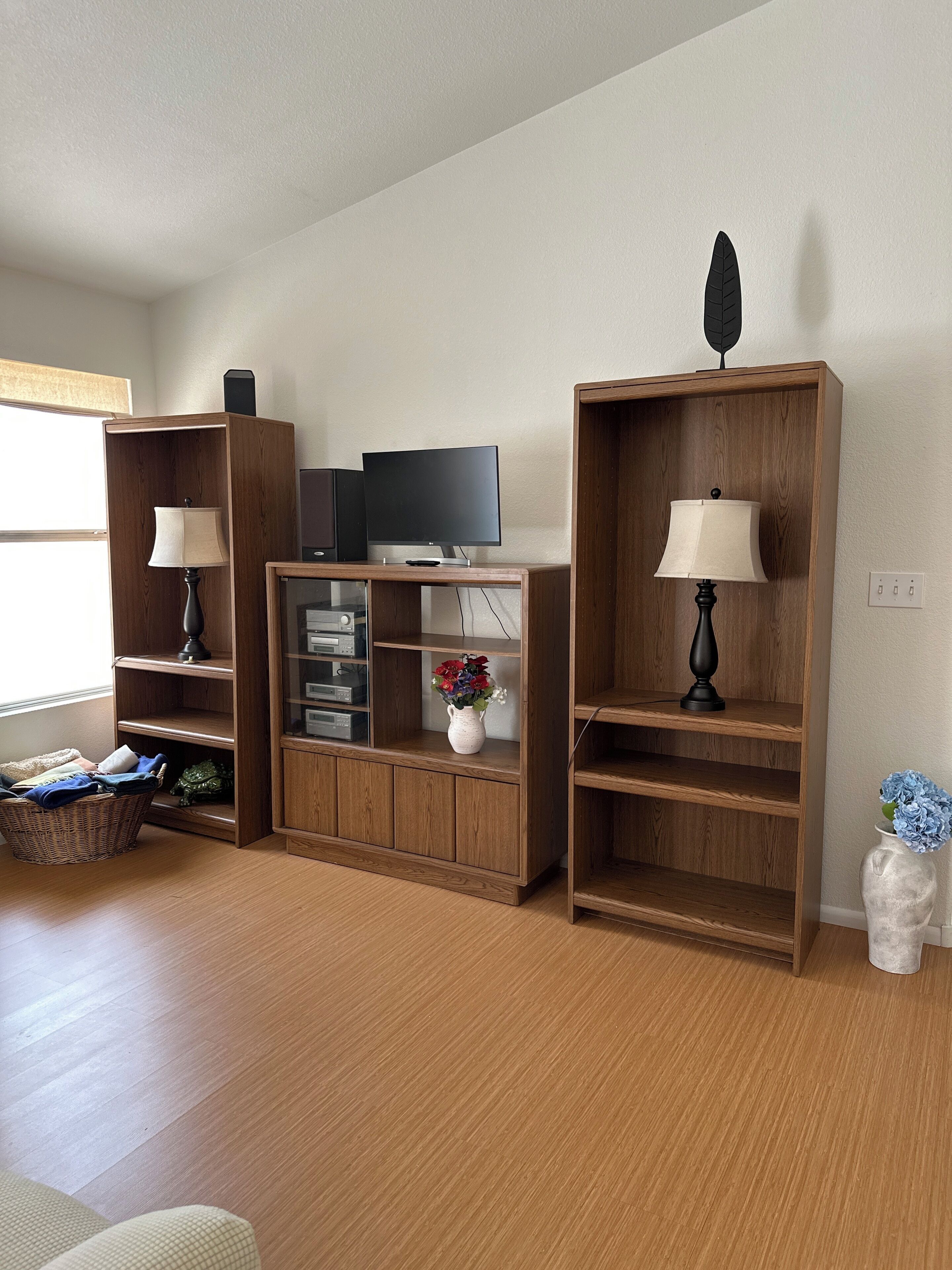 A living room with wooden shelving units, a flat-screen TV, a lamp, a vase with flowers, and a basket.