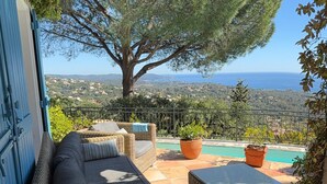 Un balcon agrémenté de meubles en osier, une vue sur la mer et un grand arbre.