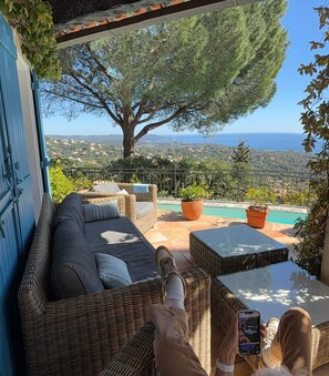 Ein Balkon mit Korbmöbeln, Blick auf das Meer und ein großer Baum.