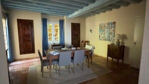 Un coin repas comprenant une table et des chaises, une fenêtre avec des rideaux et un mur orné d’un panneau décoratif.