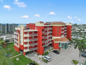 A multi-story hotel with balconies, a parking area, and a view of the sea. - Sunset Views & Endless Balcony, On Site Heated Pool and Spa, Steps to Beach (Treasure Island)