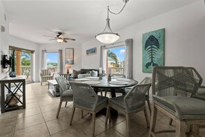 A spacious dining area with a round table, wicker chairs, and a ceiling fan.