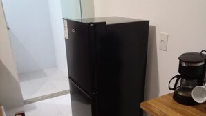 A compact kitchen with a black refrigerator, a wooden table with a coffee maker, and a tiled floor. - Suite with kitchen, well located. (Barra Velha)