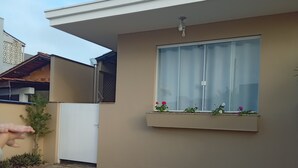 A modern building with a flat roof, a large window with a curtain, and a small balcony with plants. - Suite with kitchen, well located. (Barra Velha)