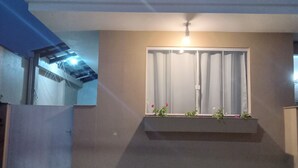 A modern building with a flat roof, a window with curtains, and a small balcony with plants. - Suite with kitchen, well located. (Barra Velha)