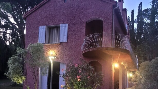 Une maison à deux étages dotée d’un balcon, entourée d’un jardin agrémenté de rochers et de plantes.