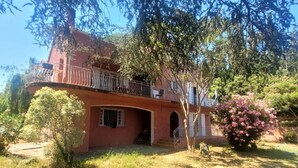 Un bâtiment à deux étages doté d’un balcon, d’une petite entrée et d’un jardin agrémenté d’arbres et d’arbustes.