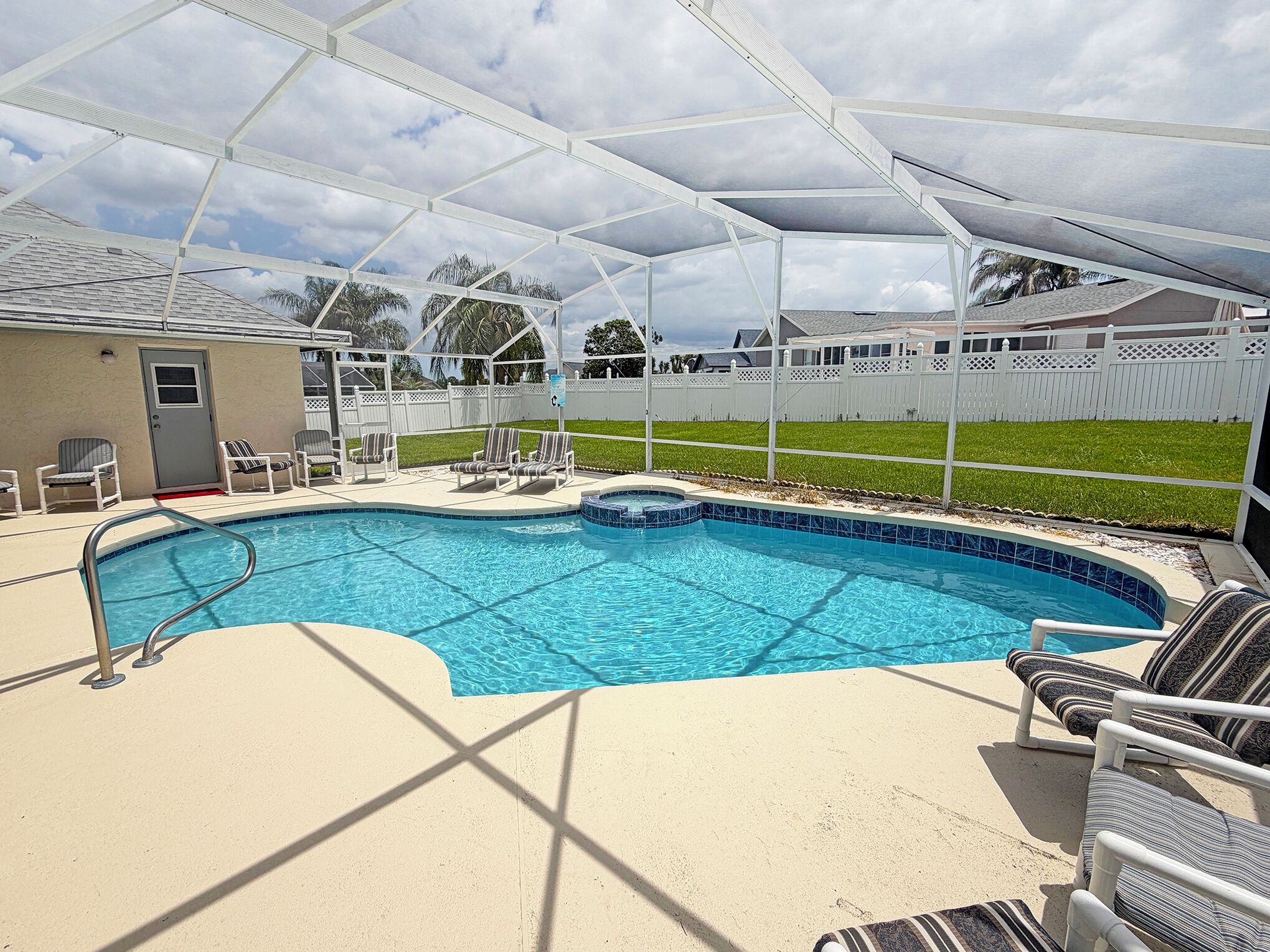A swimming pool with a covered area, lounge chairs, and a fenced yard.