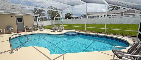 A swimming pool with a covered area, lounge chairs, and a fenced yard.