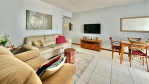 Ein Wohnzimmer mit Sofa, Fernseher, einem Holz-TV-Schrank und einem Essbereich mit Stühlen.