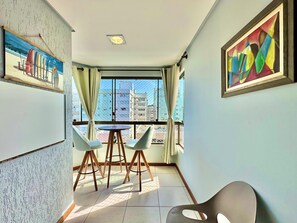 Quarto com varanda, uma mesa de jantar com cadeiras e duas pinturas nas paredes.