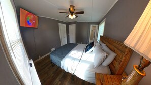 Ein Schlafzimmer mit Bett, Deckenventilator, Holz-Kopfstütze, Nachttisch und einem an der Wand montierten Fernseher.
