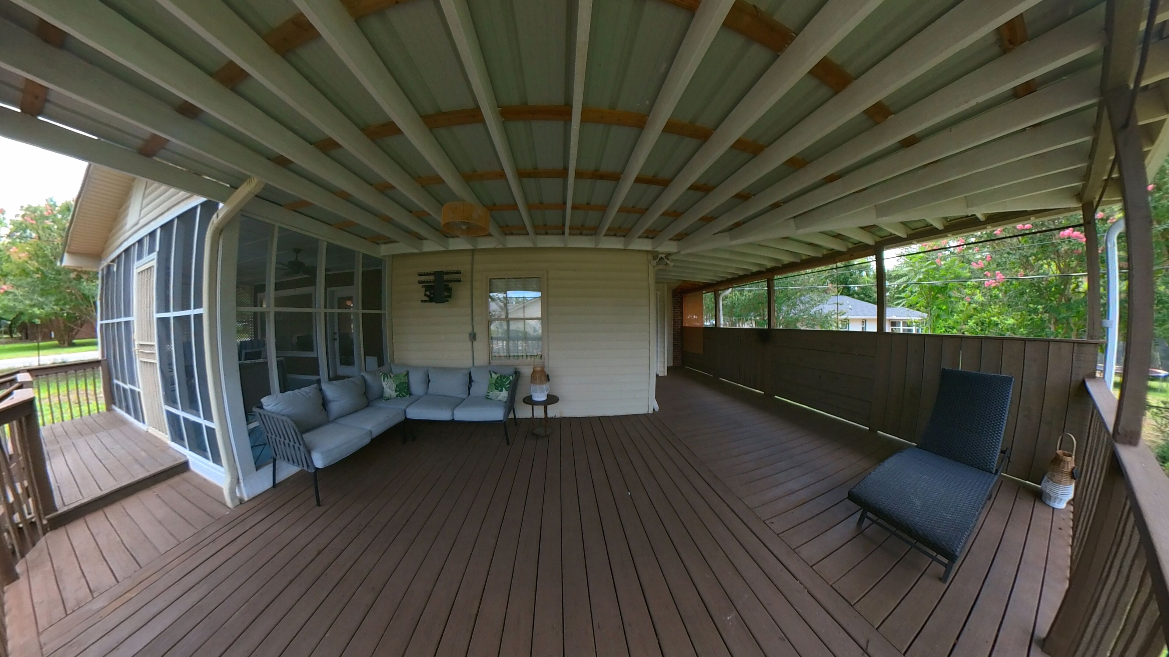 A covered outdoor deck with a wooden floor, a sofa, a chair, and a small table.
