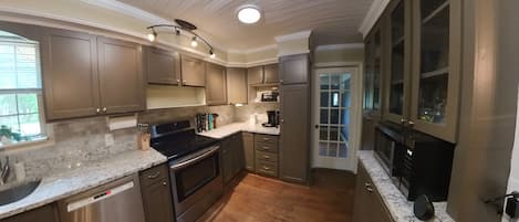 A kitchen with wooden cabinets, a stainless steel dishwasher, a black stove, and a marble countertop.