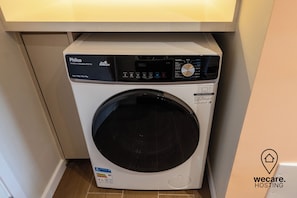 A compact, front-loading washing machine with a digital control panel, placed under a kitchen cabinet.