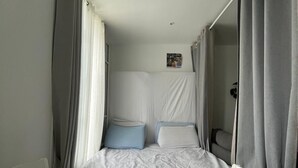 En säng med en vit madrass och kuddar, ett litet sängbord och en väggmonterad lampa.
