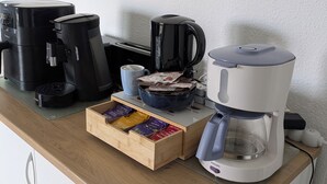 Una encimera de cocina con cafetera, tostadora, un bol de periódicos y un cajón con cápsulas de café.