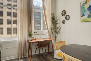 A room with a wooden desk, a chair, a potted plant, and a dining table with chairs. - New 2BR Skywalk Apt+Downtown Indy+Sleeps 7 (Indianapolis)