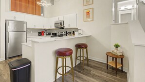 A modern kitchen with white cabinets, stainless steel appliances, and two stools. - New 2BR Skywalk Apt+Downtown Indy+Sleeps 7 (Indianapolis)