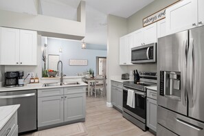 A modern kitchen with stainless steel appliances, a coffee maker, and a dining area with a table and chairs. - 3BR Home with Private Pool Minutes from Disney (Kissimmee)