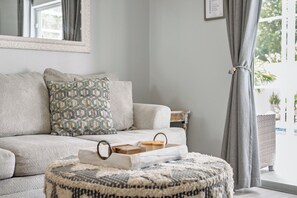 A living room with a sofa, patterned pillows, a round ottoman, and a window with curtains. - 3BR Home with Private Pool Minutes from Disney (Kissimmee)